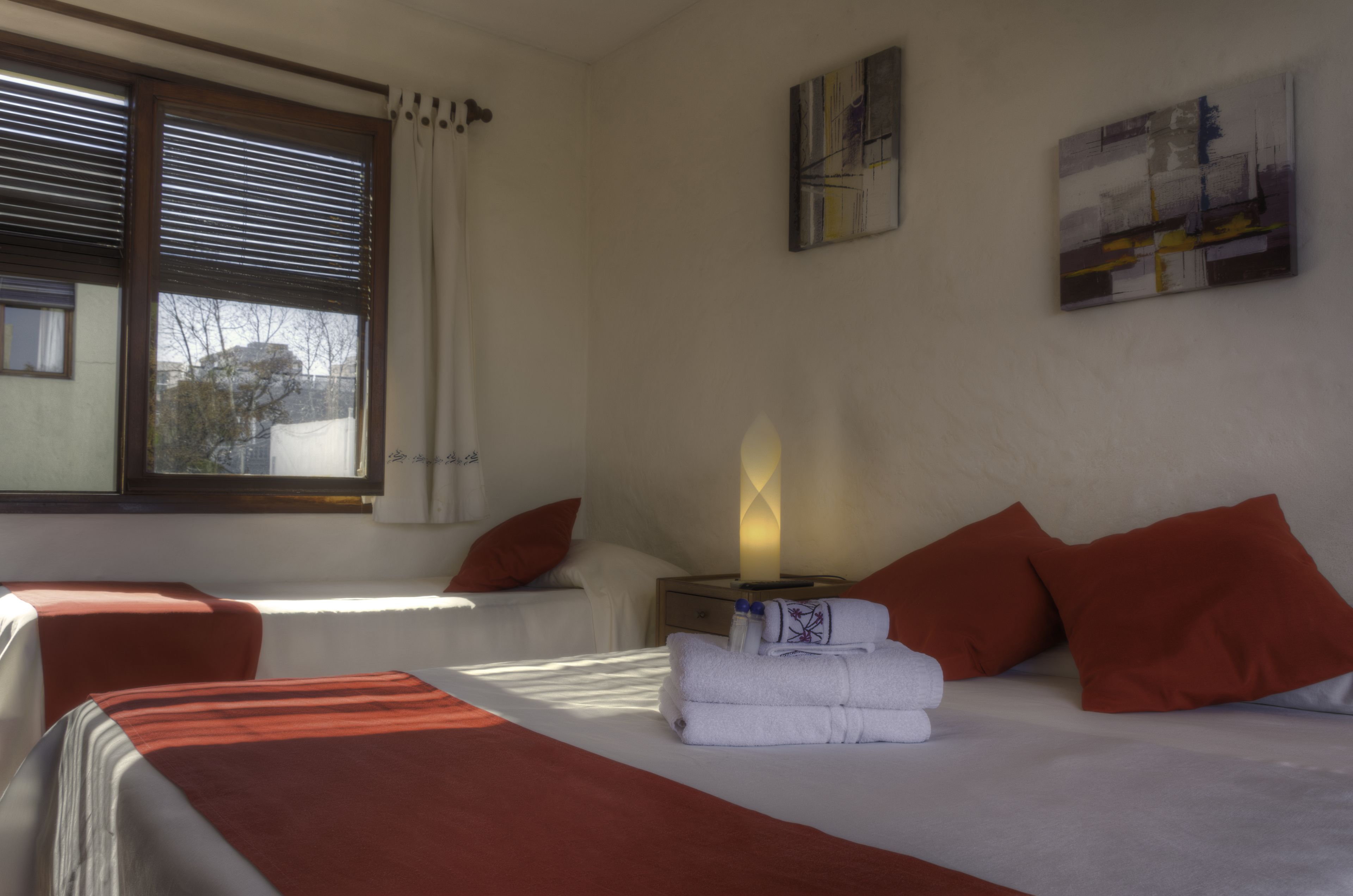 Quarto de hotel com duas camas, uma mesa de cabeceira com abajur e uma janela com persianas.