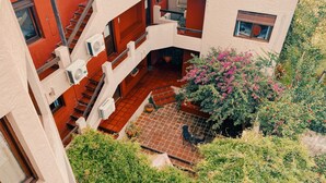 Edificio de varios niveles con escalera, unidades de aire acondicionado y un patio con plantas en macetas y un árbol en flor.