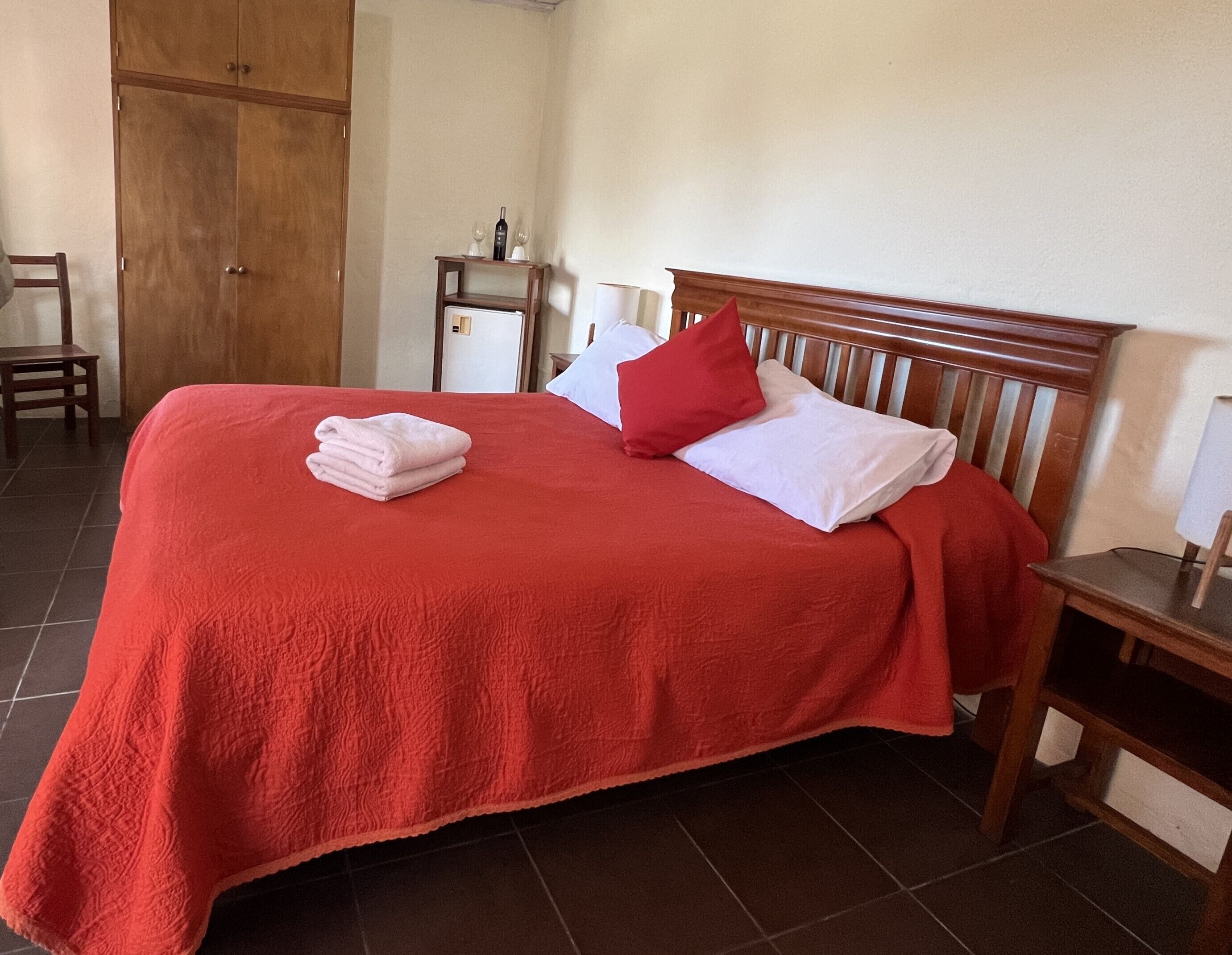 A neatly made bed with a red bedspread, white pillows, and a folded towel.