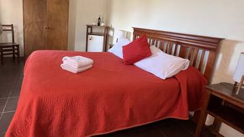 A neatly made bed with a red bedspread, white pillows, and a folded towel.
