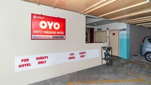 A hotel entrance with a sign for OYO SWITZ PARADISE HOTEL, a guest-only sign, and a parking area with a car.