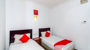 A hotel room with two beds, white bedding, red pillows, a wall-mounted light, and a power outlet.