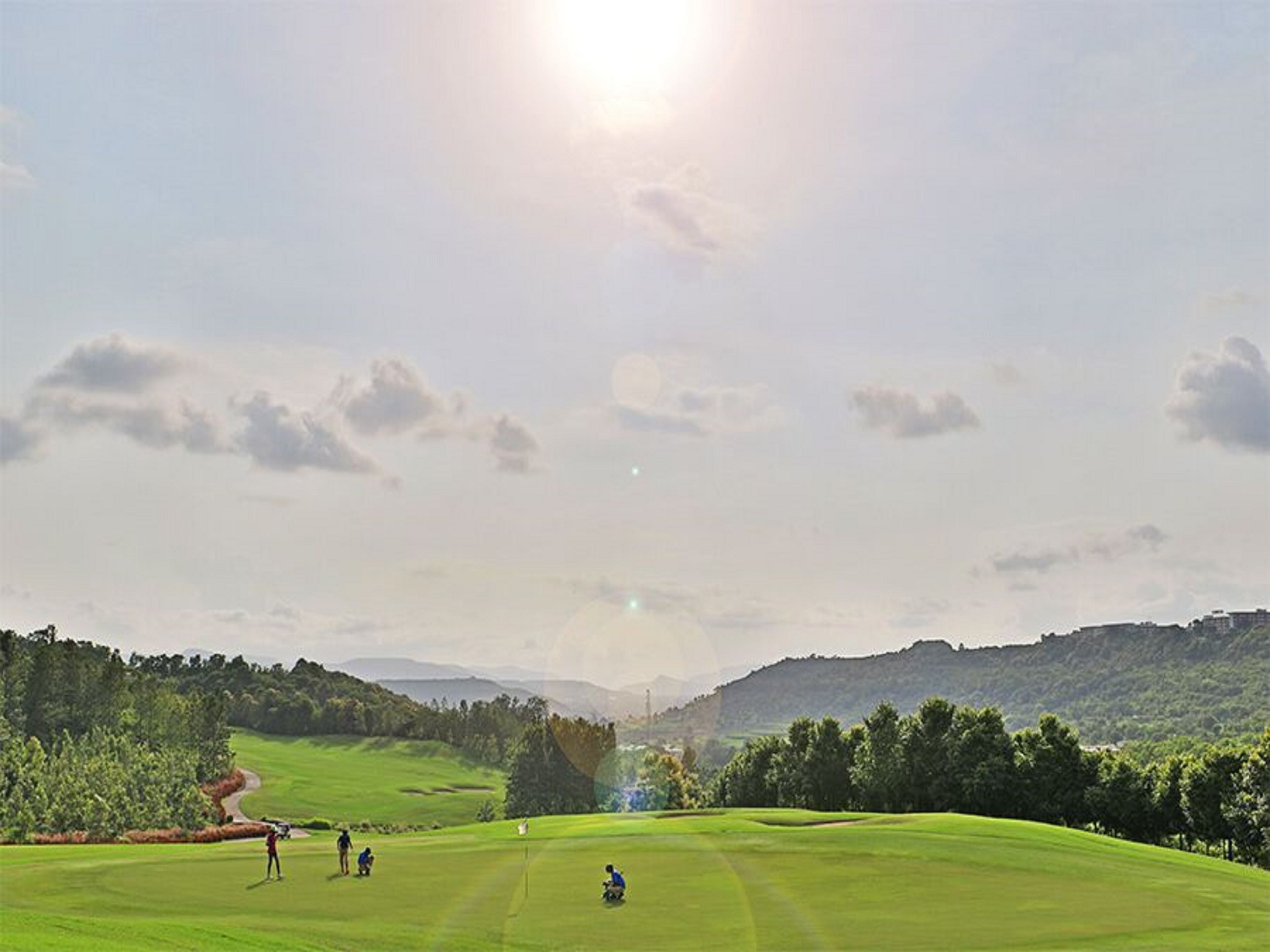 A golf course with a clear sky, distant hills, and a few golfers.