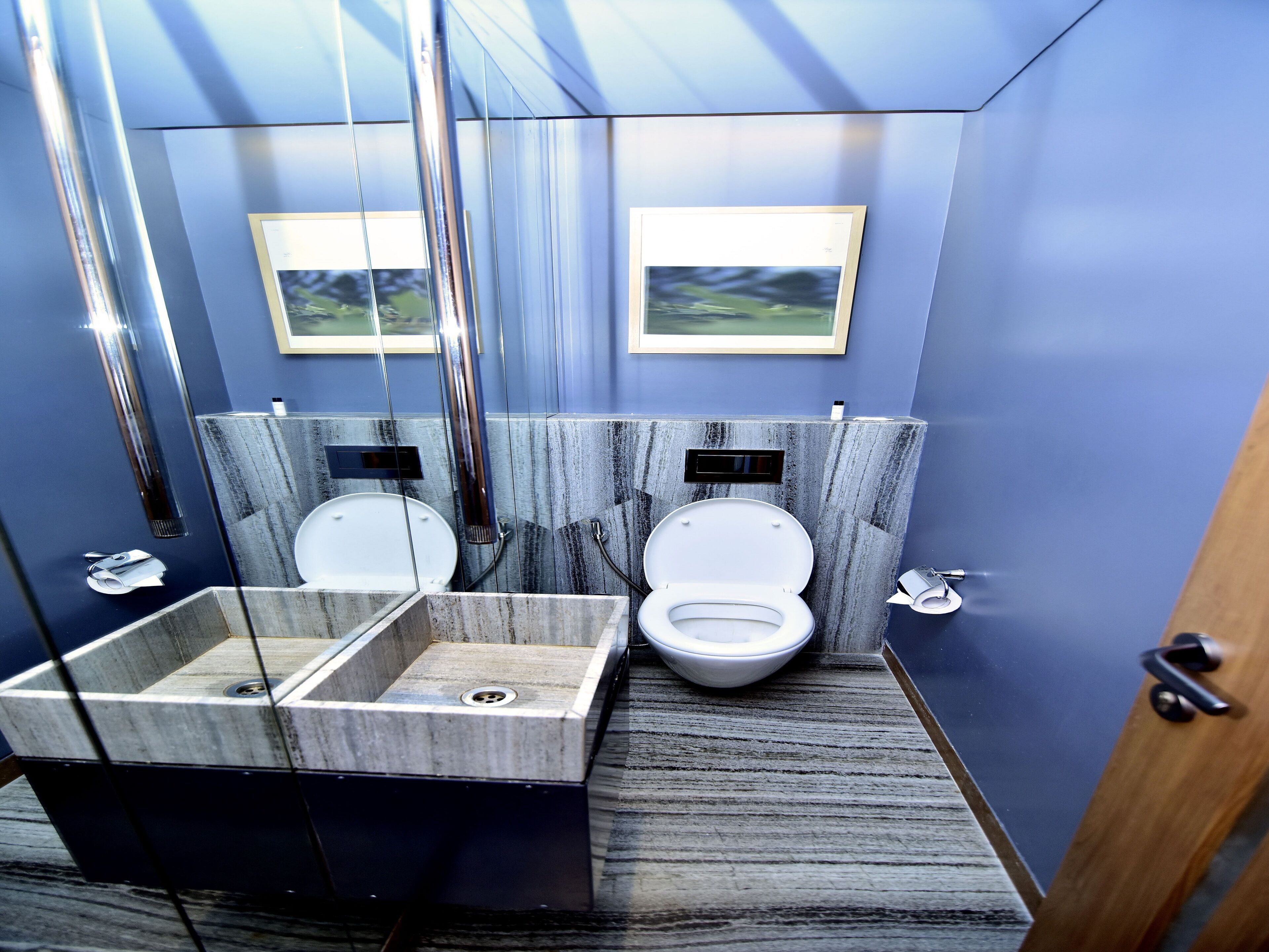 A modern bathroom with a marble sink, two toilets, and a wooden floor.