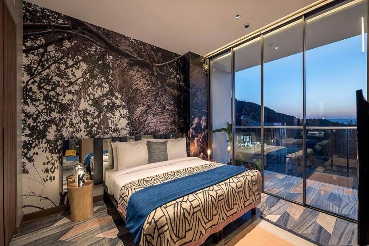 A modern bedroom with a large bed, a view of the outdoors, and a unique wall design.