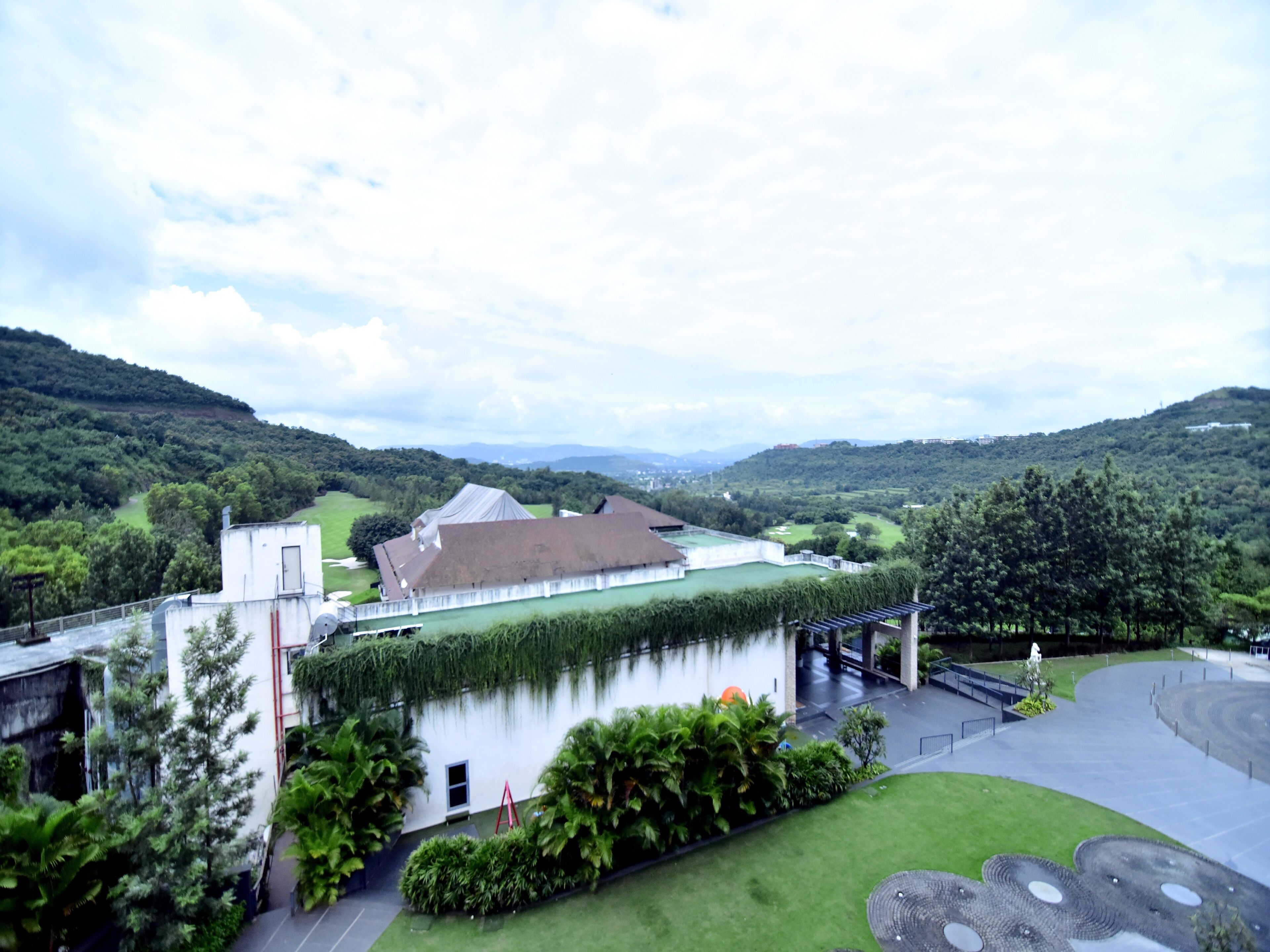 A building with a green roof and a white facade, surrounded by lush greenery and hills.