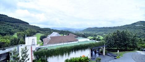 A building with a green roof and a white facade, surrounded by lush greenery and hills.