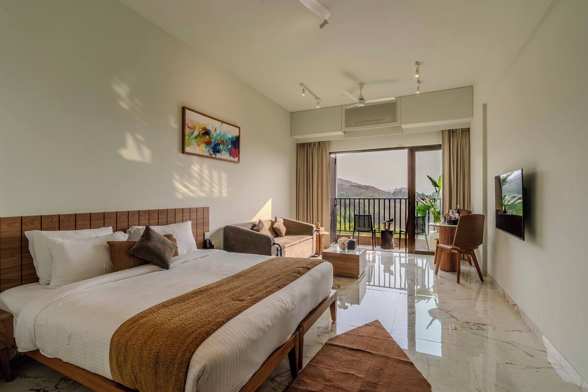 A hotel room with a large bed, a balcony with a view, a TV, and a dining area.