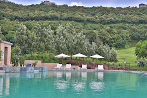 Una piscina con sillas de descanso y sombrillas, rodeada de exuberante vegetación y un campo de golf al fondo.