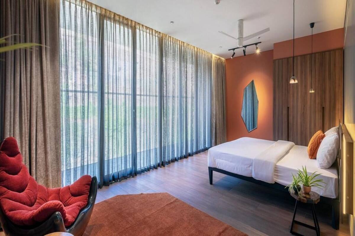 A bedroom with a bed, a red chair, a large window with curtains, and a ceiling fan.
