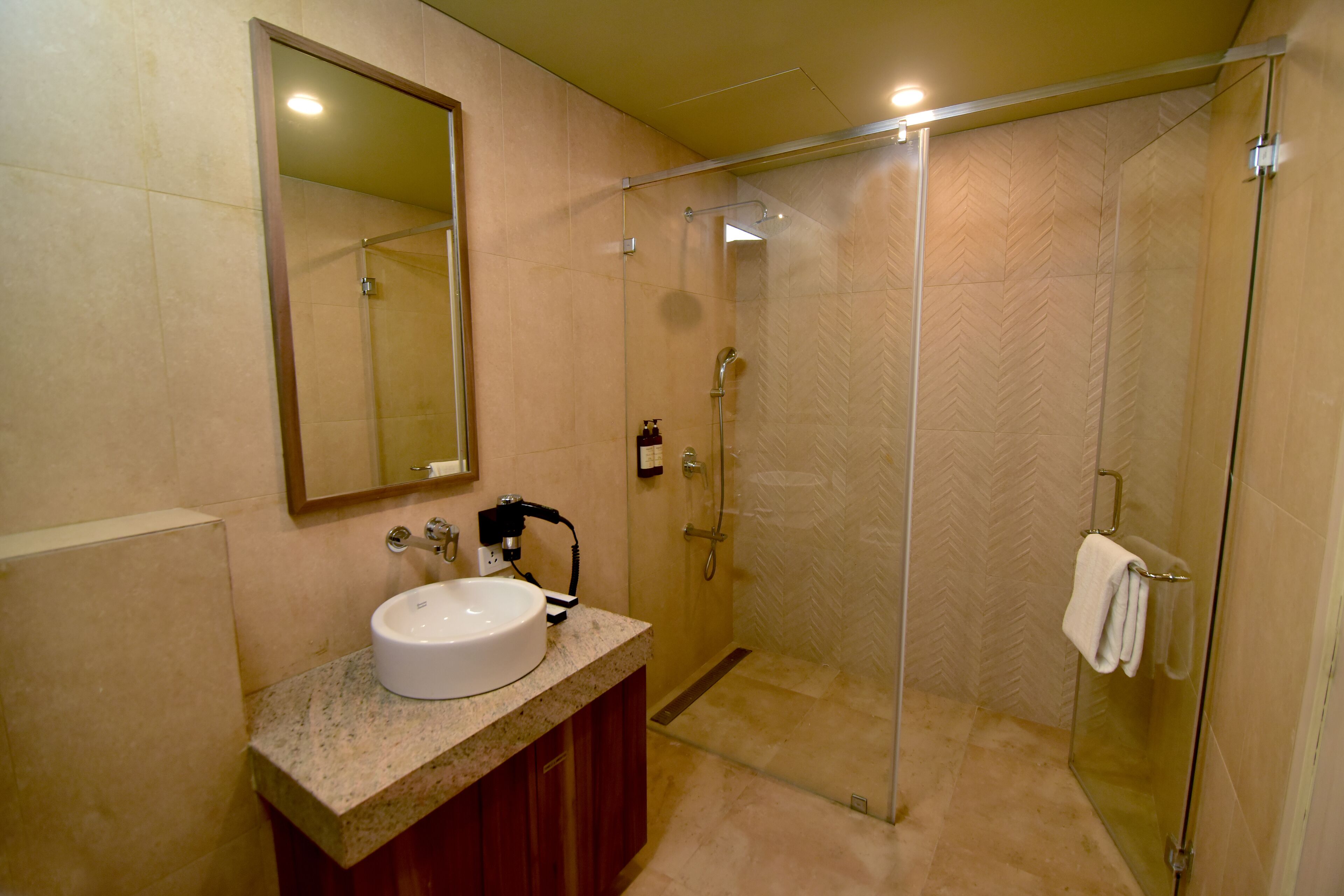 Casa de banho com cabine de duche em vidro, lavatório com bancada de mármore e espelho sobre o lavatório.