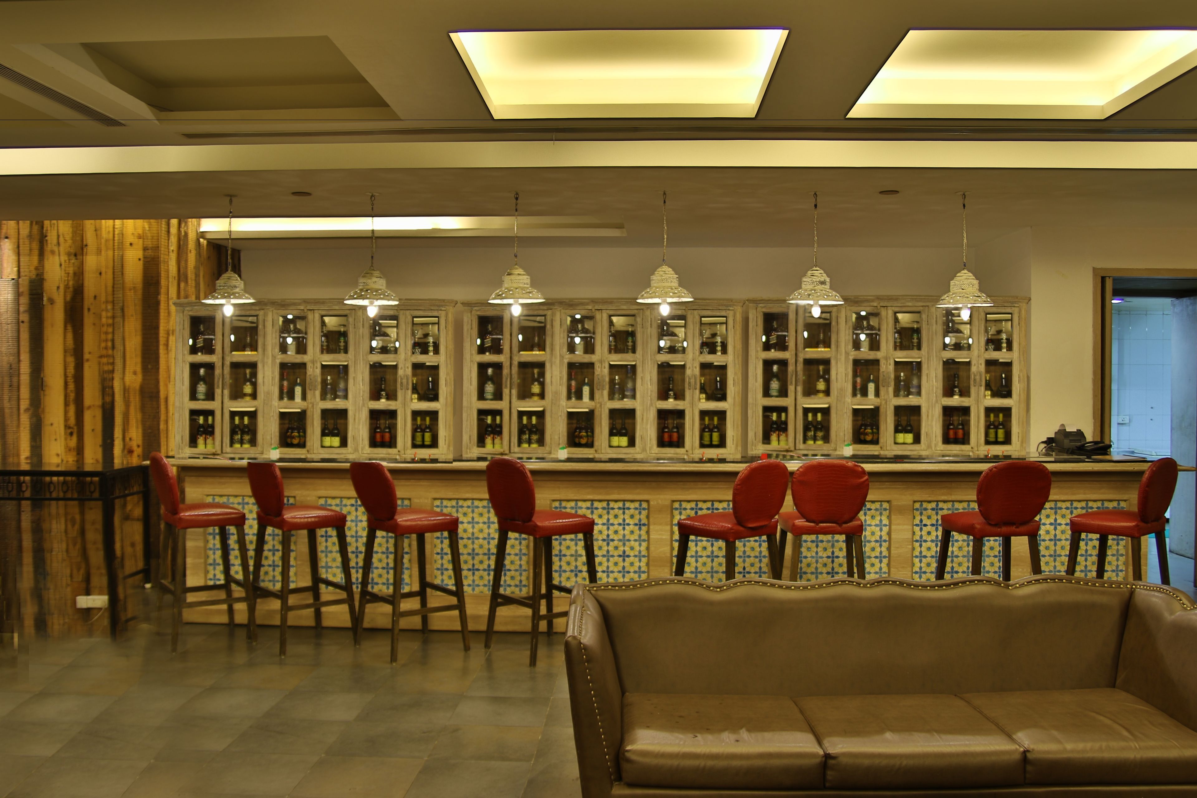 A bar area with red bar stools, a brown leather couch, and a tiled backsplash with glass-fronted cabinets.