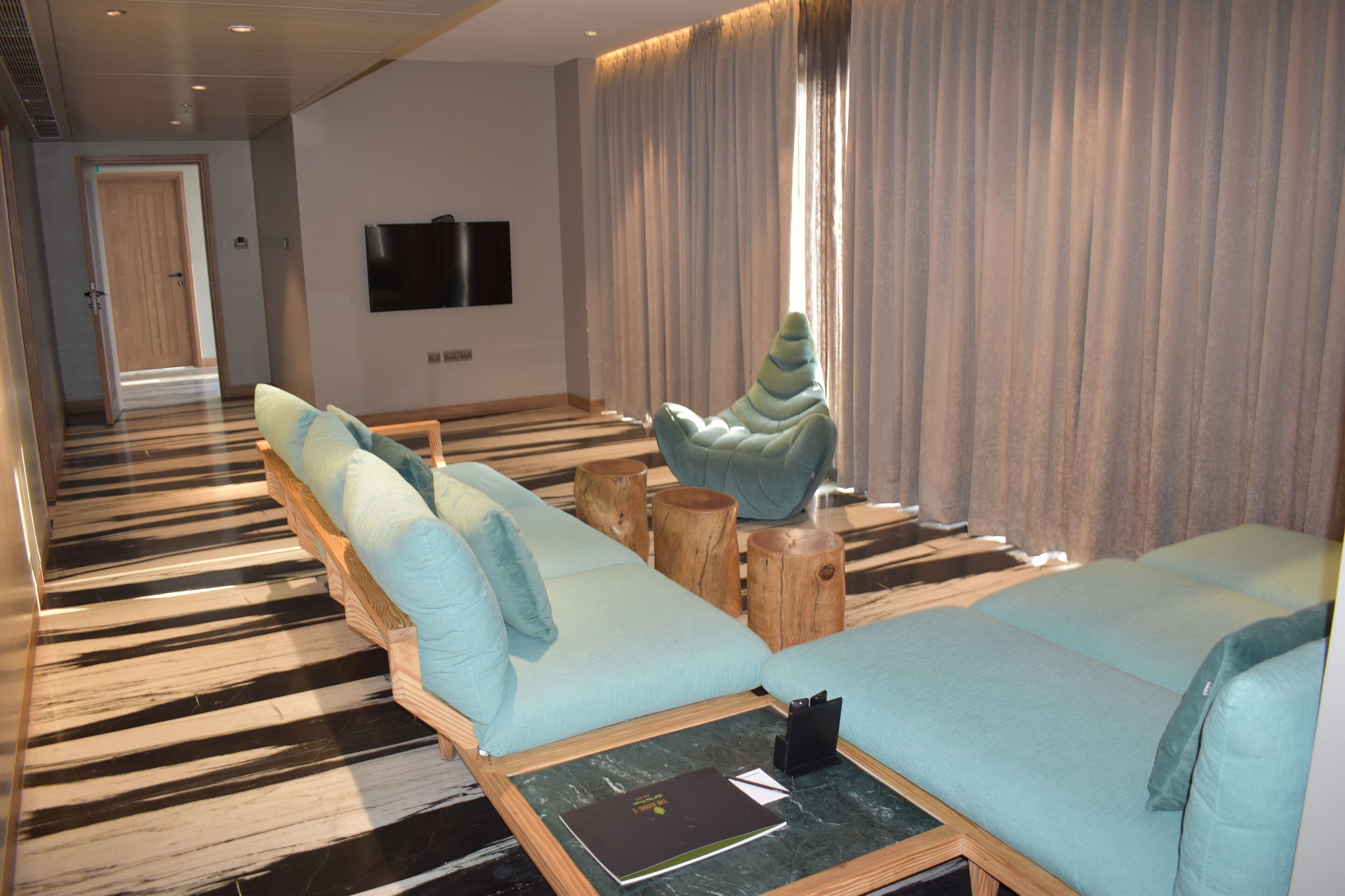 A modern hotel room with a striped floor, a sofa set, a wooden coffee table, and a television on the wall.