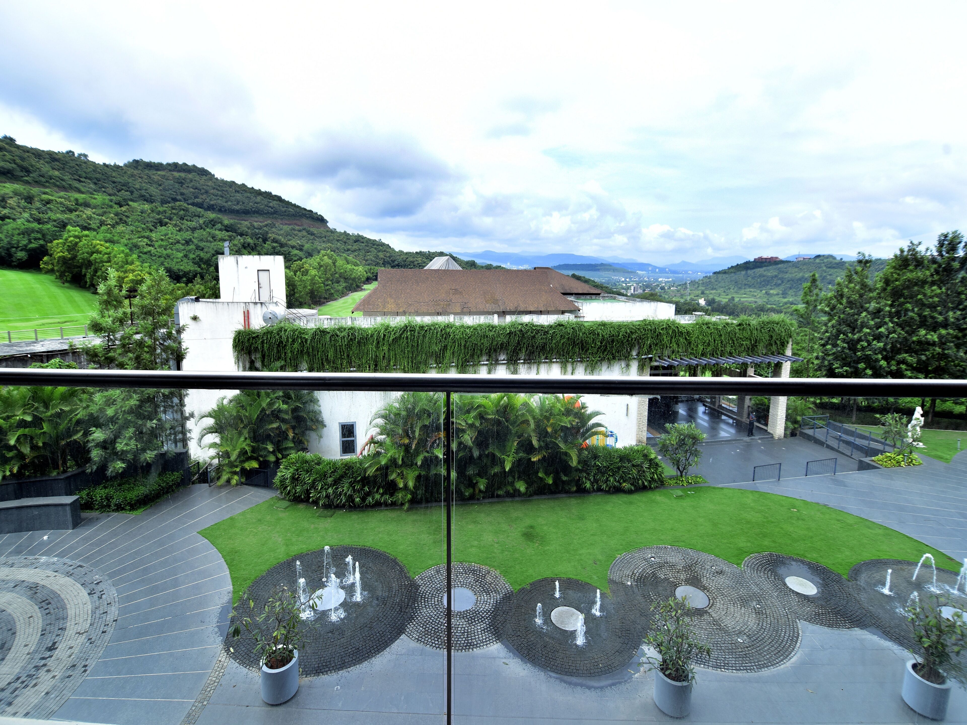 A courtyard with a fountain, a white building with a green roof, and a view of the surrounding hills.