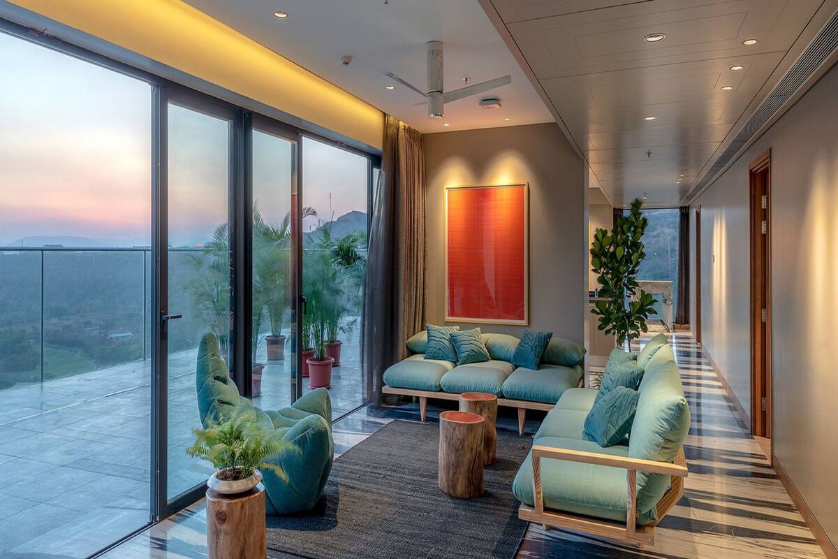 A spacious living area with a large sliding glass door leading to a balcony, a modern sofa set, and a large abstract painting on the wall.