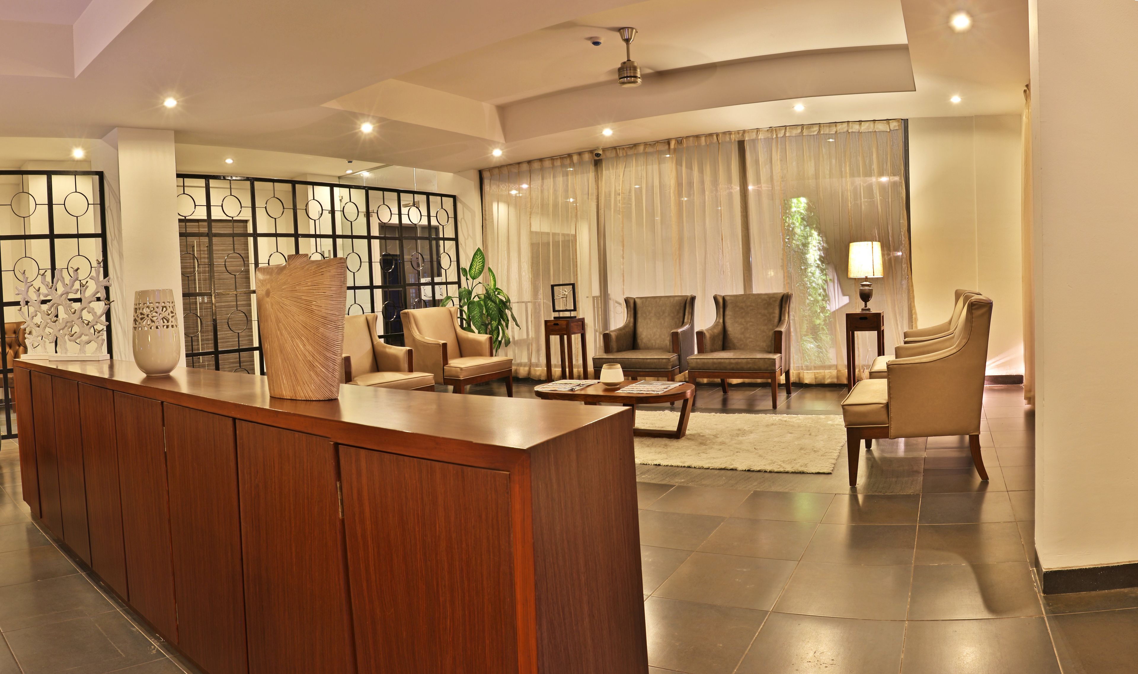 A spacious lobby with a wooden reception desk, comfortable seating, and a large window with sheer curtains.