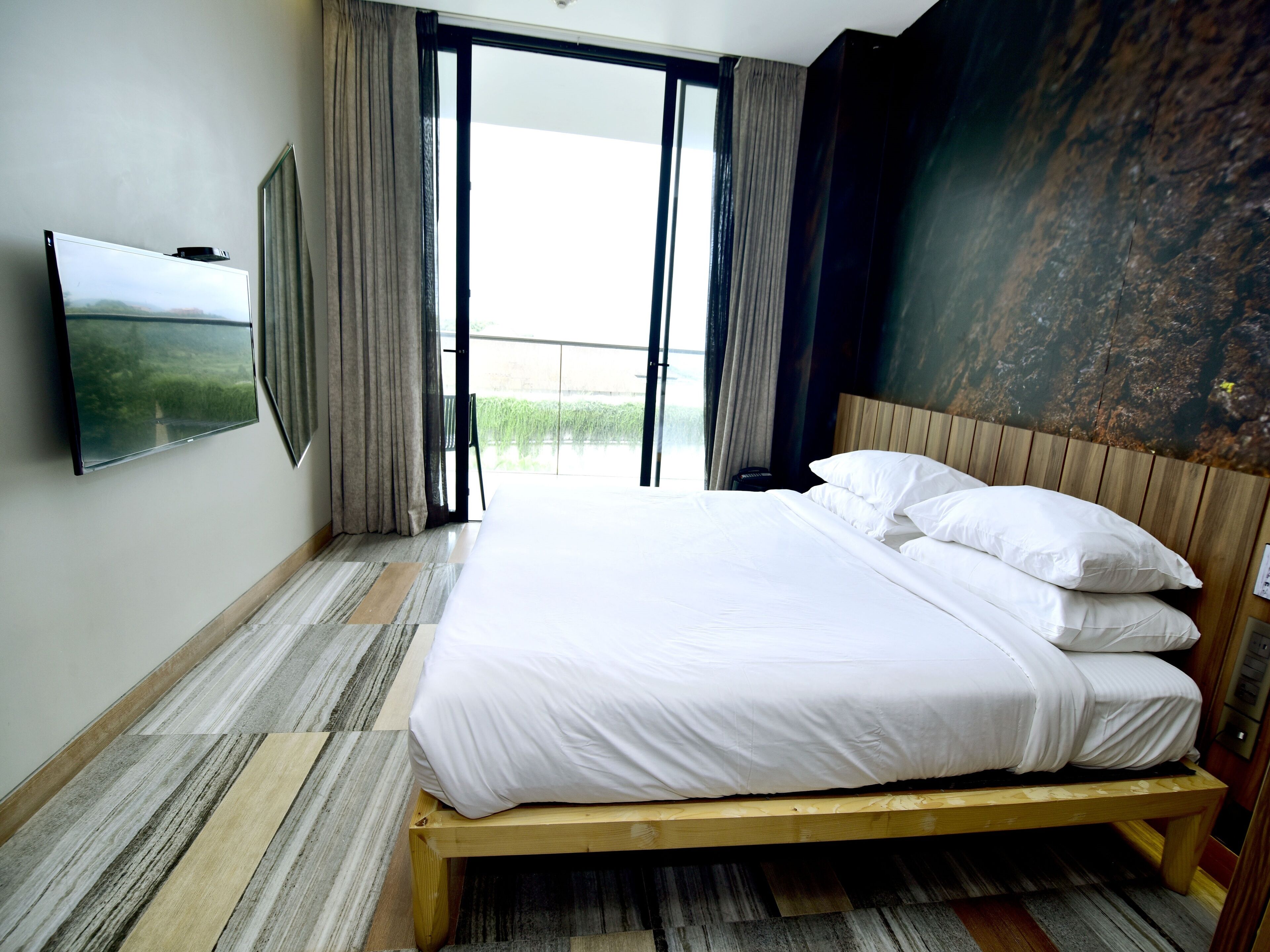 A hotel room with a large bed, a flat-screen TV, and a view through the open door.