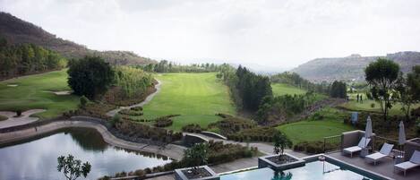 A pool with a view of a golf course and hills in the background.