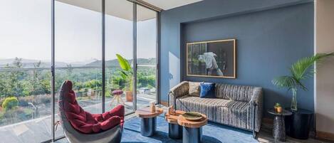 A modern living room with a large glass wall, a red chair, a grey sofa, and a blue rug.