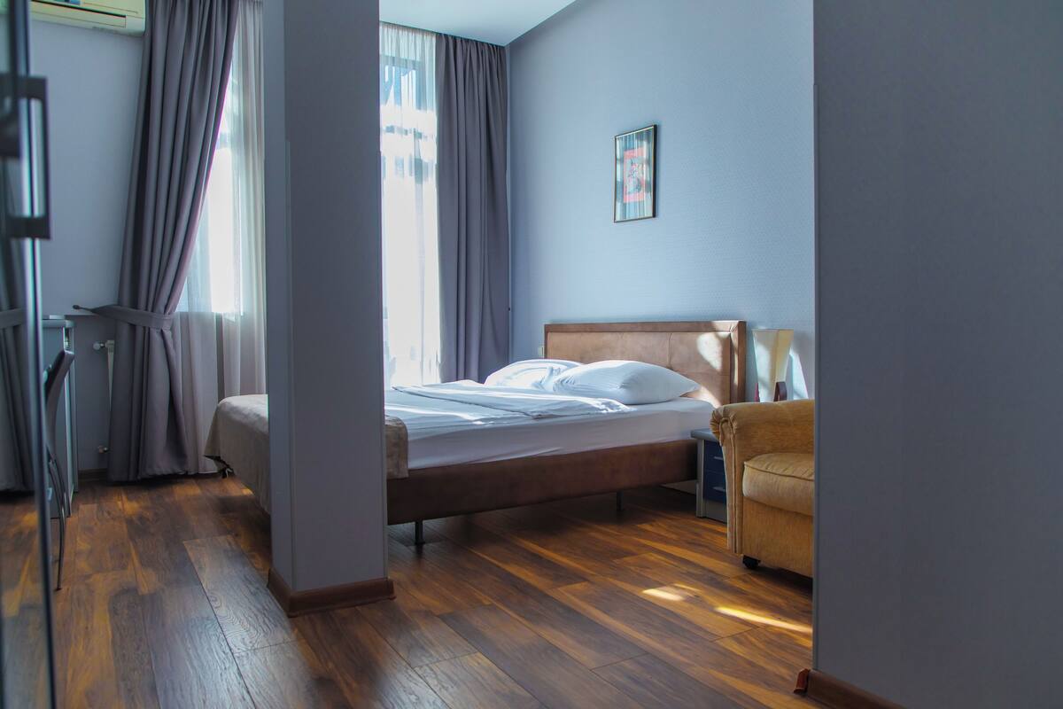 A hotel room with a wooden bed, a chair, a desk, and a window with curtains.