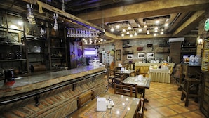 Una zona de bar con mesas y sillas de madera, una barra con una máquina de café y lámparas colgantes.