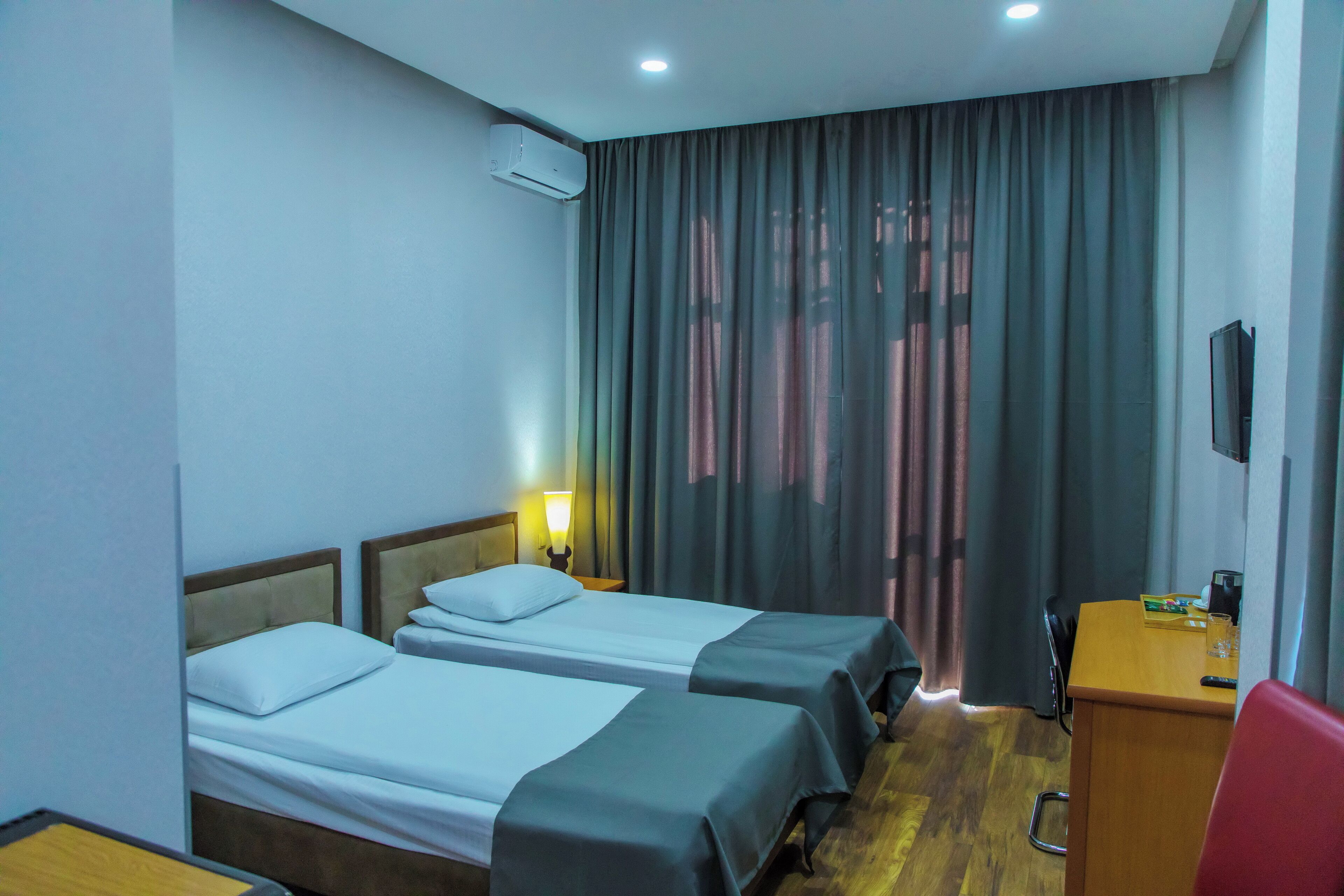 A hotel room with two beds, a desk, a chair, a TV, and a window with curtains.