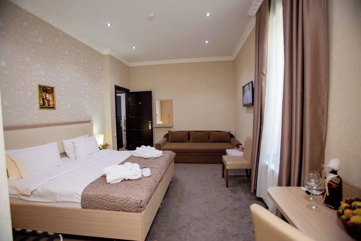 A hotel room with a bed, a sofa, a desk, a chair, and a dining table.
