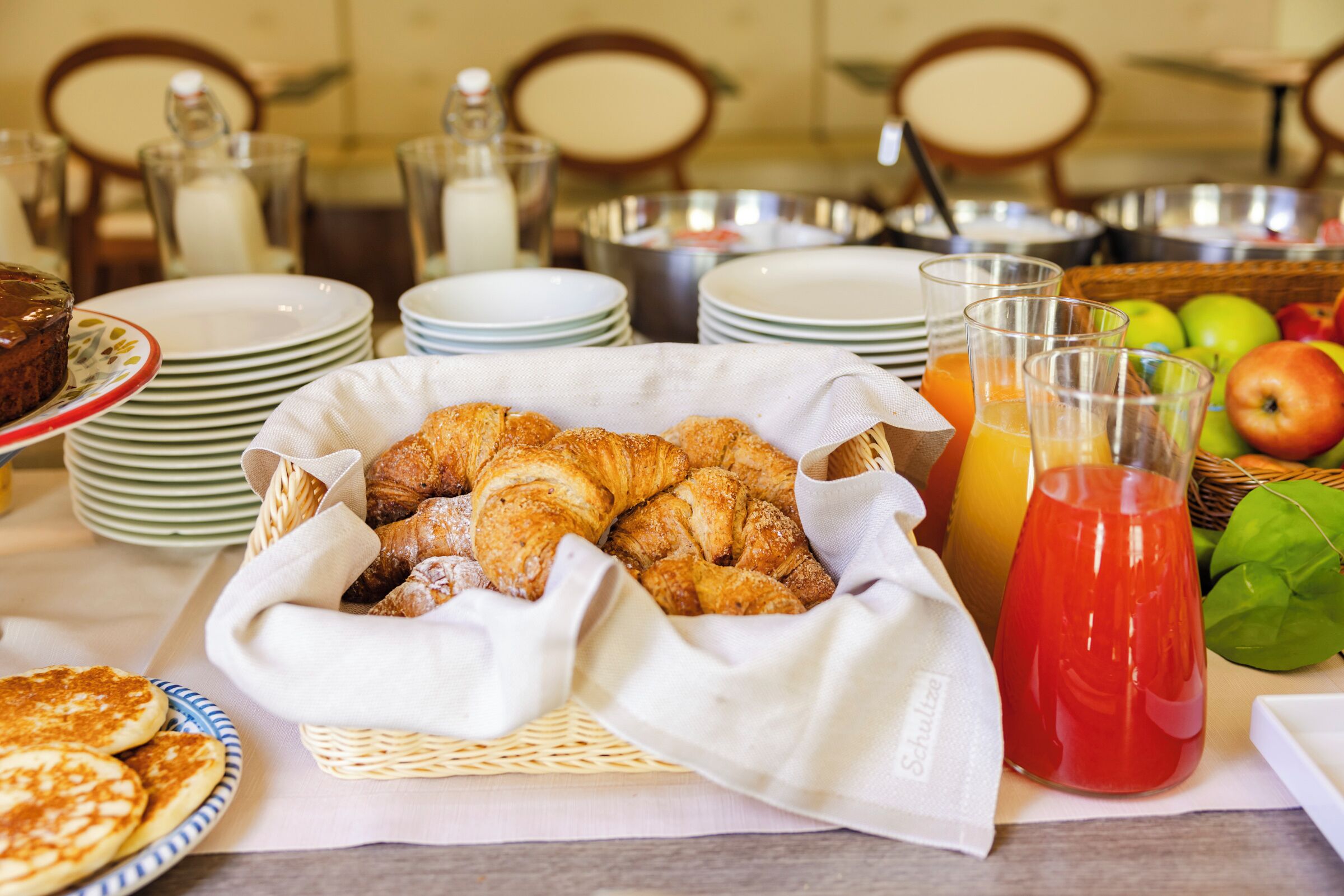 A breakfast buffet with croissants, pancakes, and juice.