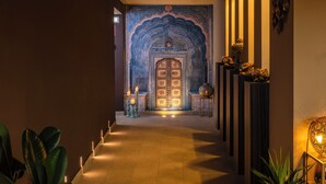 A hallway with a decorative archway leading to a door, a row of plants on the left, and a wall-mounted lamp on the right. - Il Gentiluomo Hotel & SPA (Arezzo)