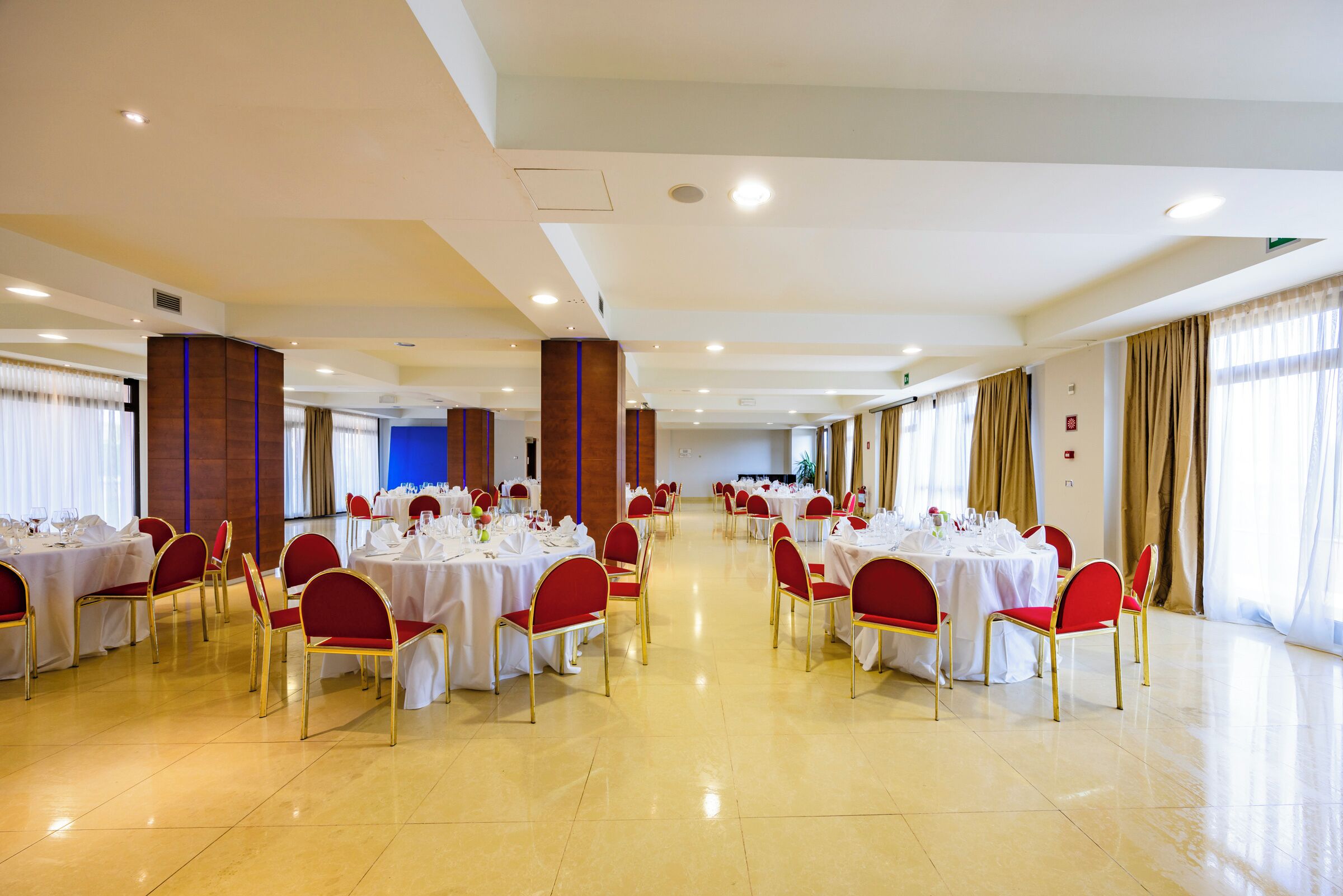 A spacious banquet hall with multiple round tables and red chairs, arranged in rows.