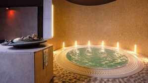A spa area with a circular hot tub surrounded by mosaic tiles, a stone bench, and a small table with a bowl and a candle. - Il Gentiluomo Hotel & SPA (Arezzo)