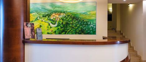 A reception desk with a large painting of a landscape, a modern light fixture, and a staircase in the background.