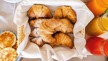 Un cestino con croissant e pancake su un tavolo, insieme a bicchieri di succo d'arancia.