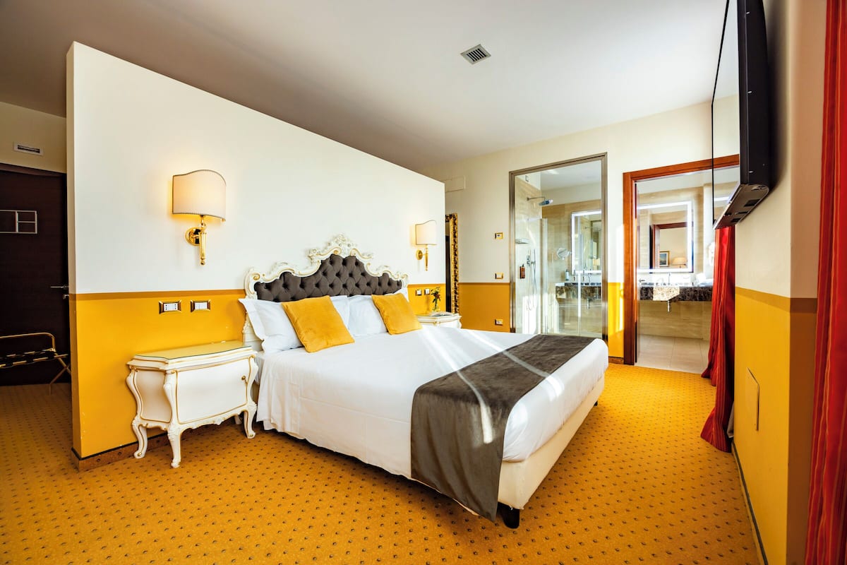 A hotel room with a large bed, two bedside tables, a wall-mounted TV, and a mirror.