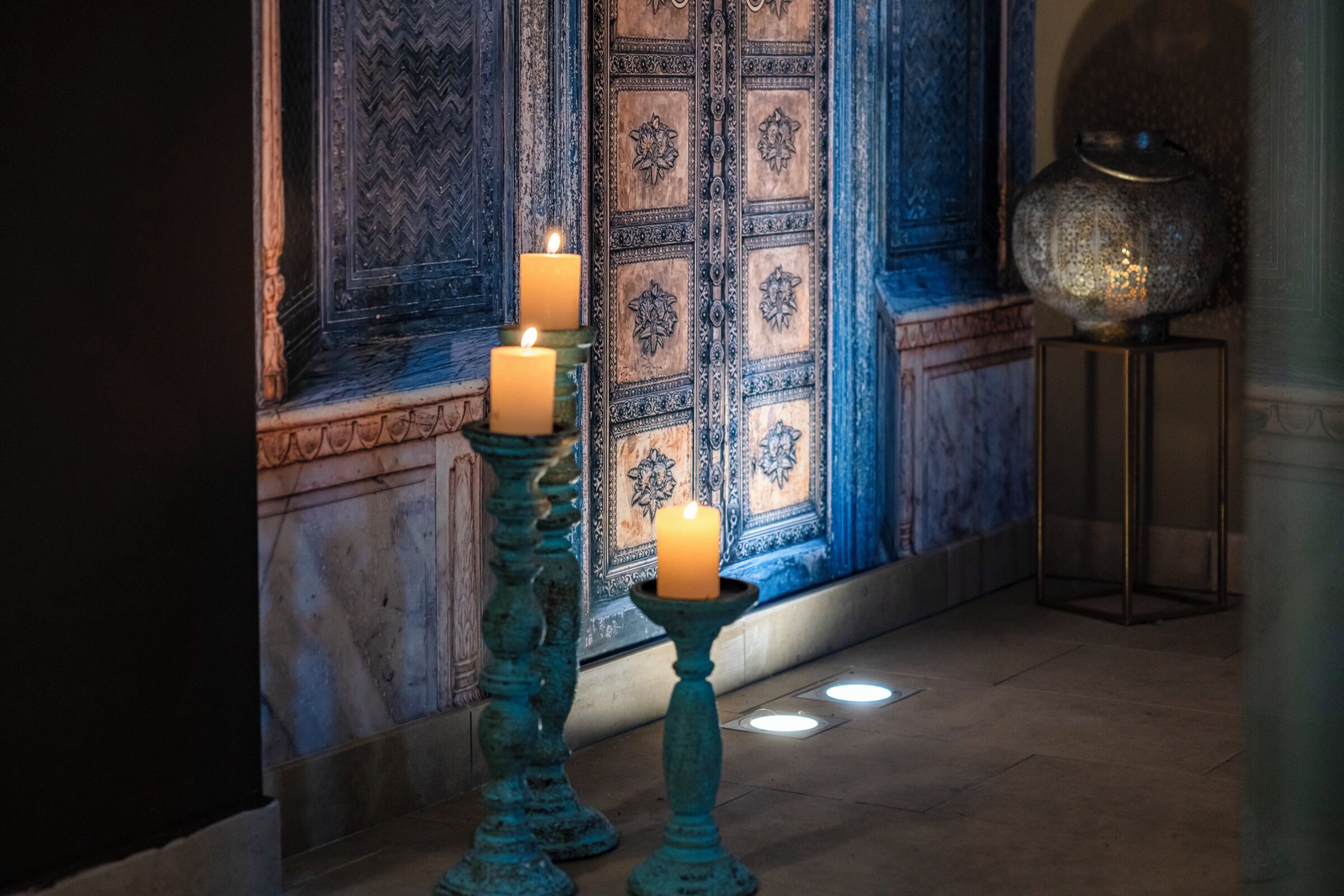 Una habitación con una puerta decorativa, dos velas sobre soportes y una lámpara de pie.