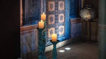 A room with a decorative door, two candles on stands, and a floor lamp.