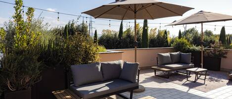 An outdoor patio area with a sofa, two chairs, a small table, and two large umbrellas.