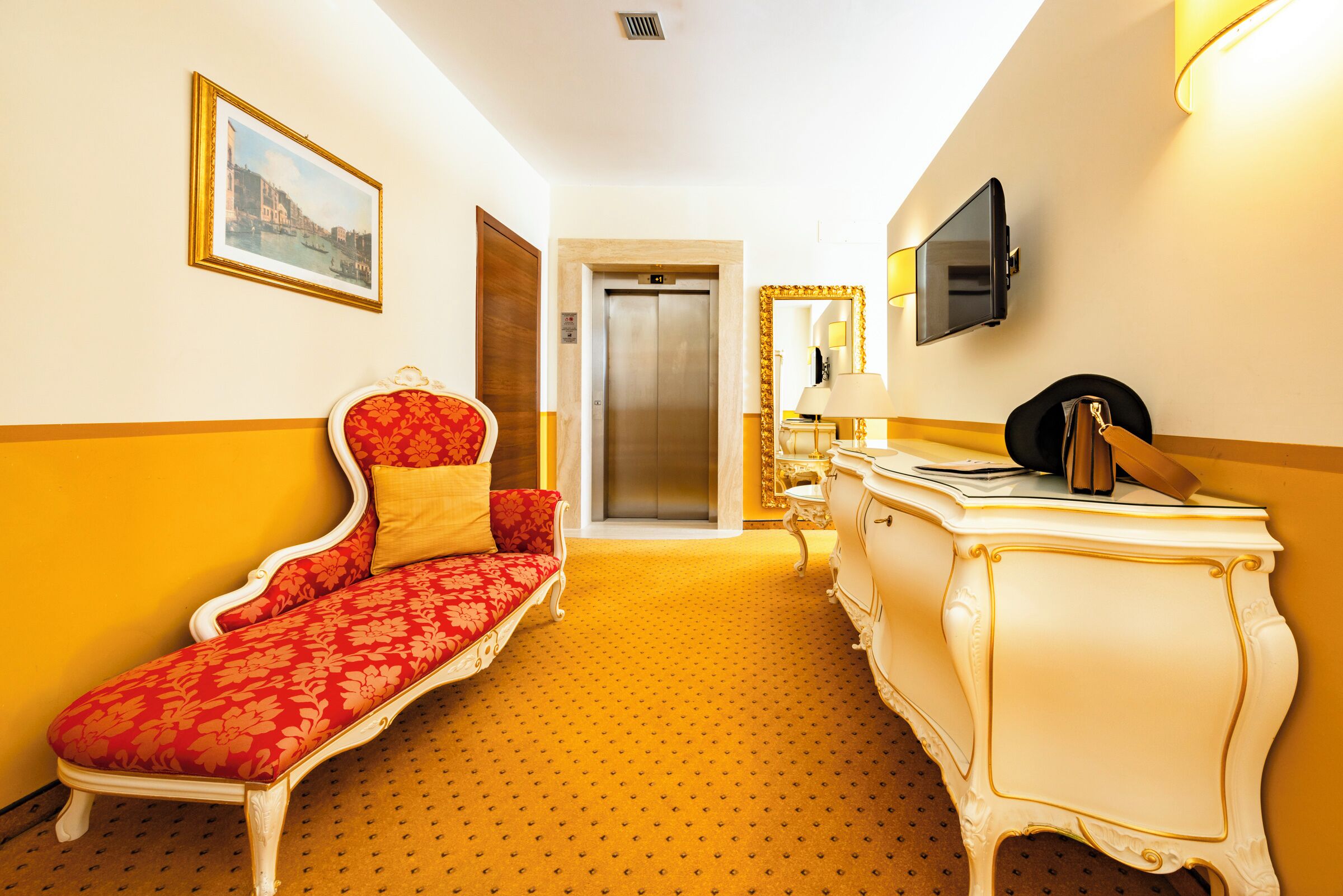 A hotel room with a red sofa, a white dresser, a mirror, a television, and an elevator.