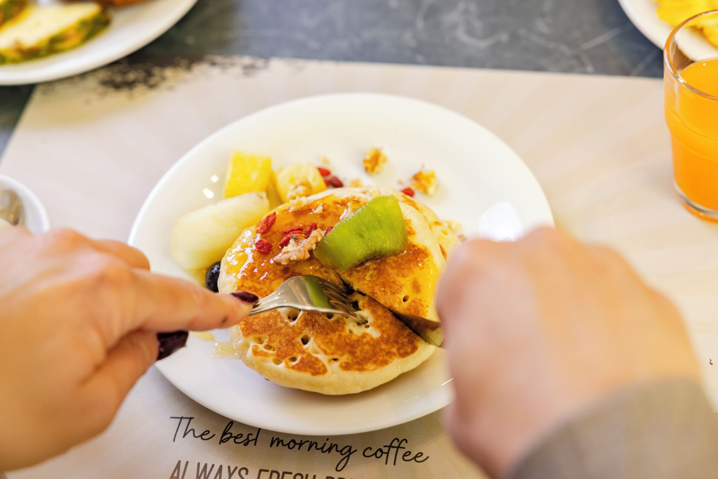 Un piatto per la colazione con pancake, frutta e un bicchiere di succo d'arancia.