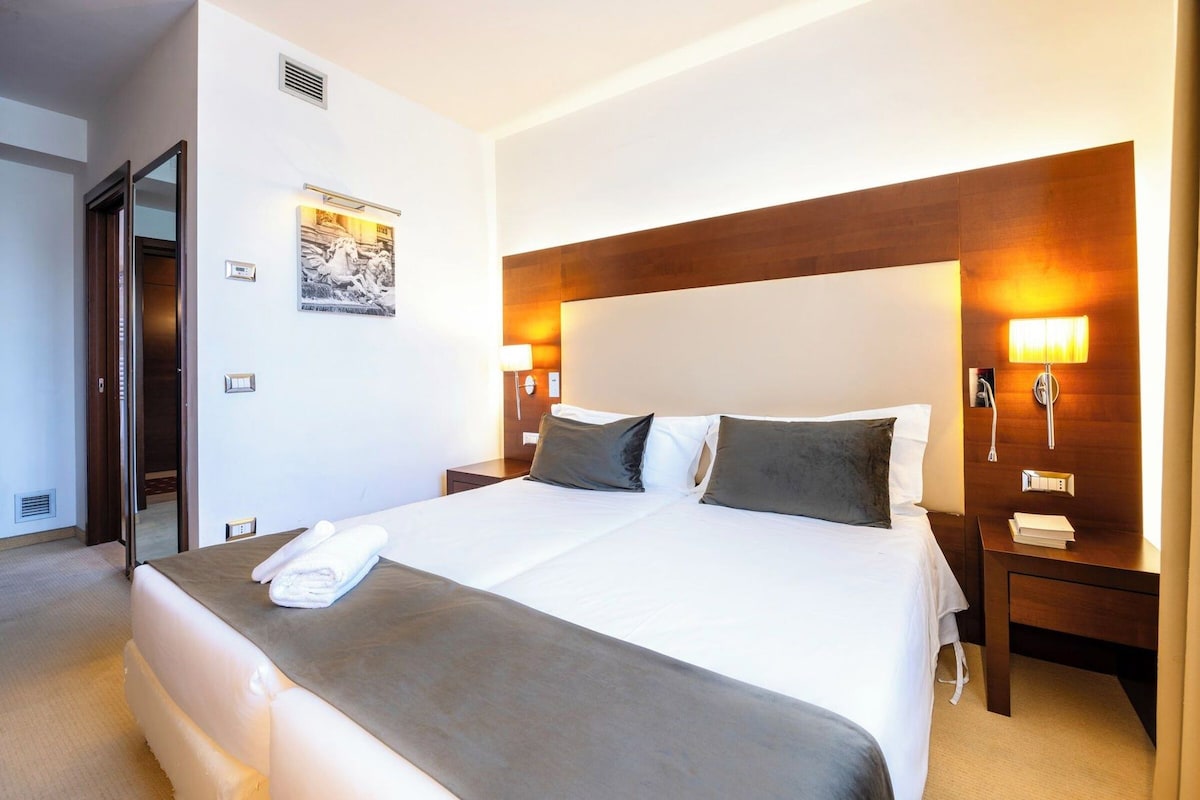 A hotel room with a large bed, two bedside tables, a wall-mounted lamp, and a poster on the wall.