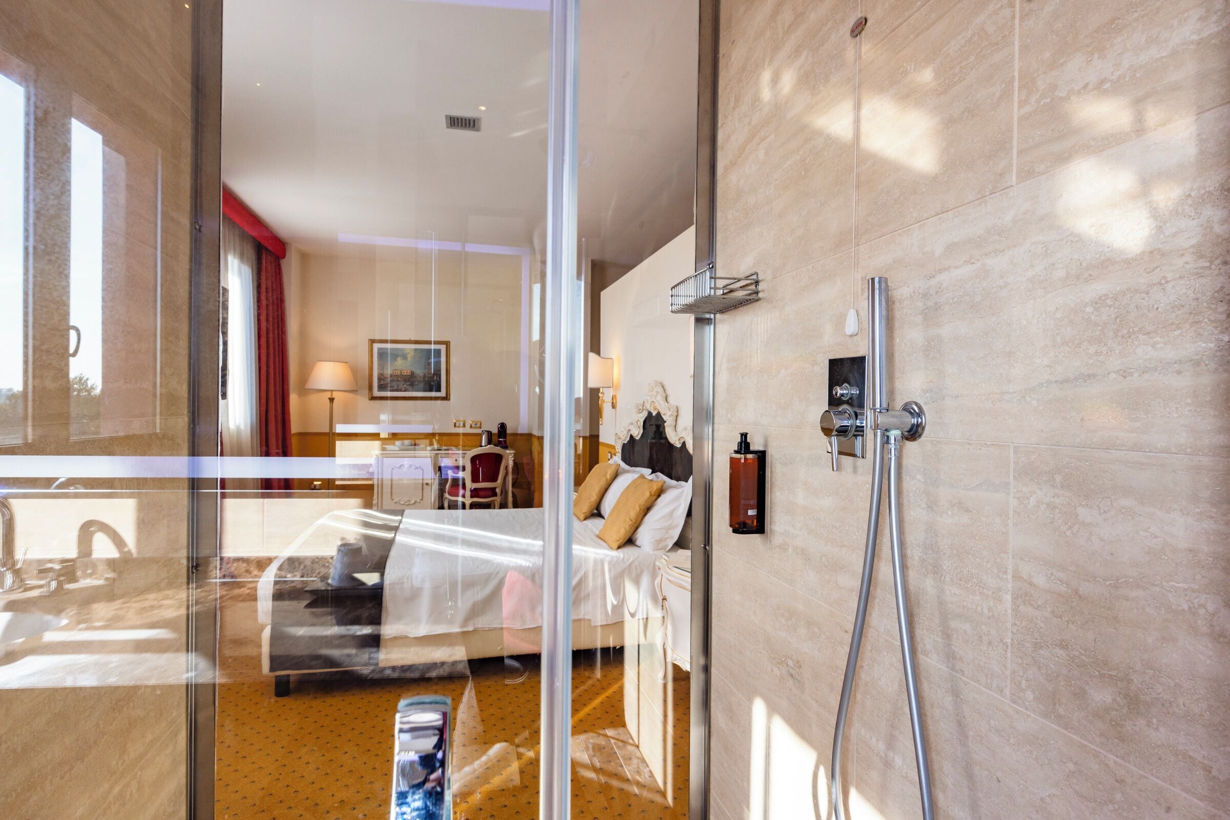 A hotel room with a bed, a shower, a desk with a chair, and a view through a glass door.