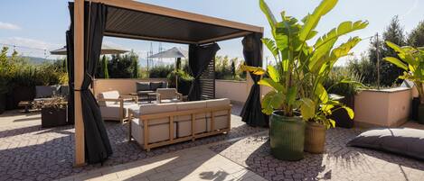 Un patio exterior con una pérgola de madera, un sofá color beige y plantas en macetas.