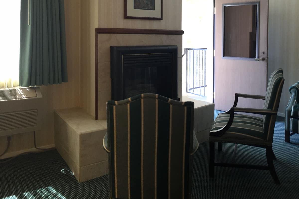 Une chambre d’hôtel avec une cheminée, deux fauteuils, une fenêtre avec des rideaux et une porte donnant sur un espace extérieur.