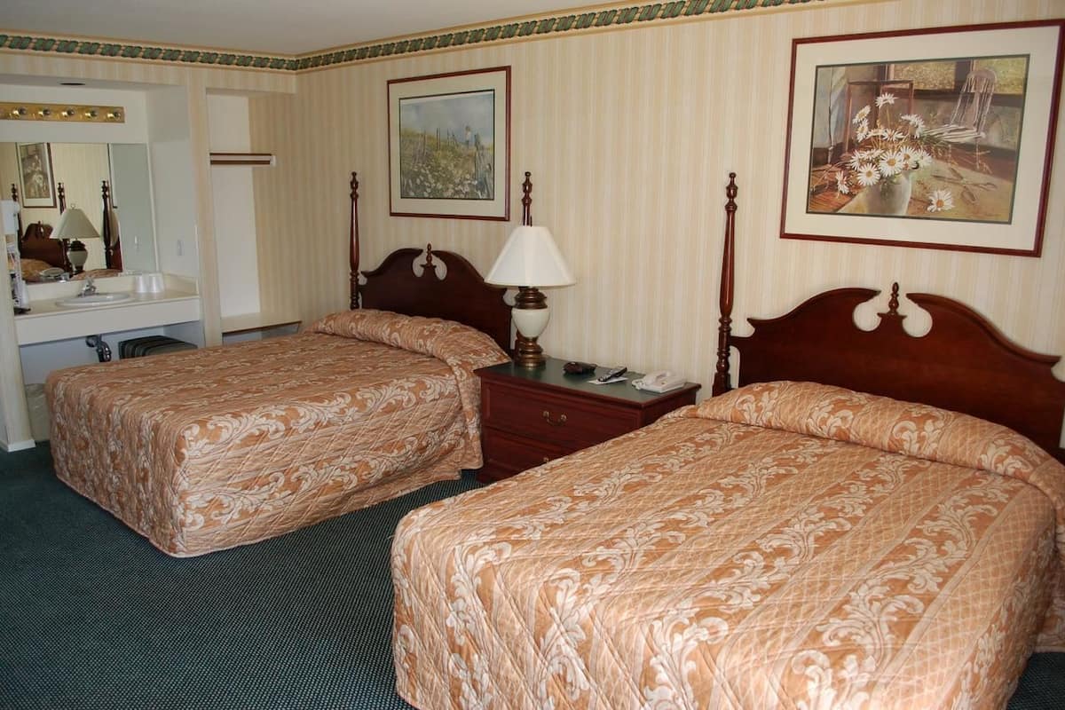 Une chambre d’hôtel avec deux lits, un grand miroir, une table de chevet avec une lampe et une commode.