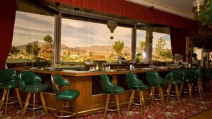 Un espace bar avec des tabourets verts, un comptoir en bois et de grandes fenêtres offrant une vue sur un paysage montagneux.