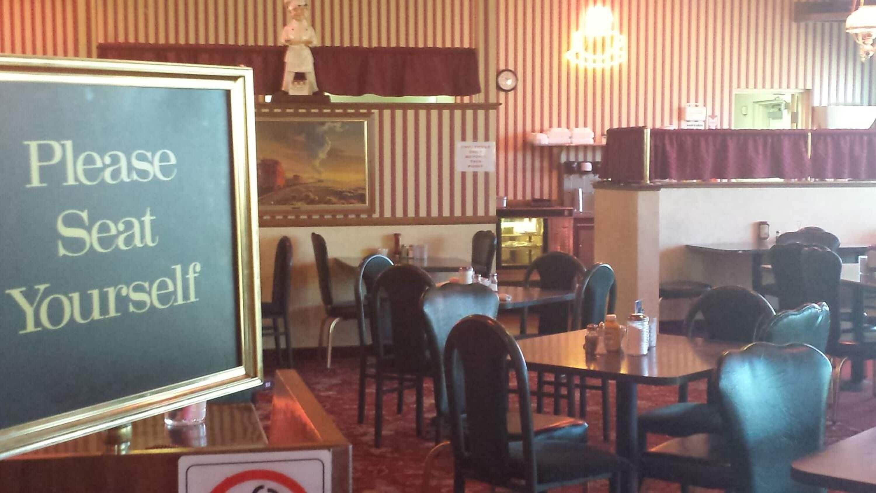 L’intérieur d’un restaurant avec des tables et des chaises, un panneau indiquant aux clients de « s’asseoir où ils le souhaitent » et un autre panneau interdisant de fumer.