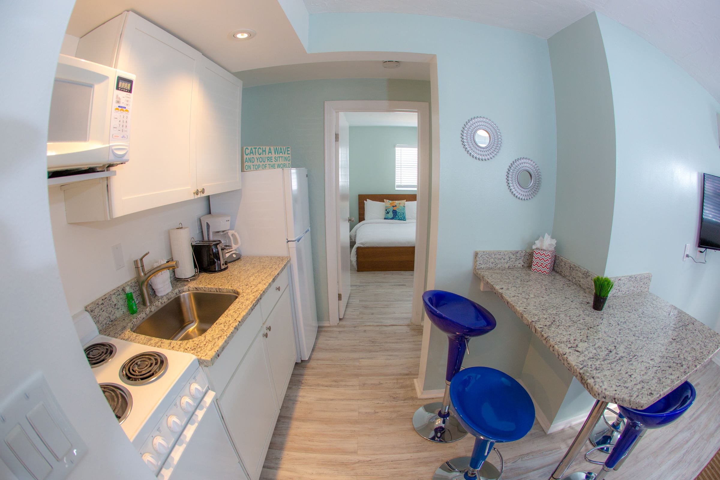 Una cocina compacta con microondas, estufa, pileta y taburetes de bar.