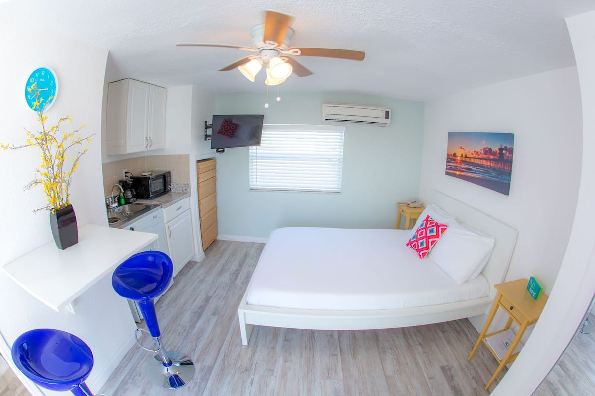 Une petite pièce comprenant un lit, une kitchenette, un ventilateur de plafond et une fenêtre.