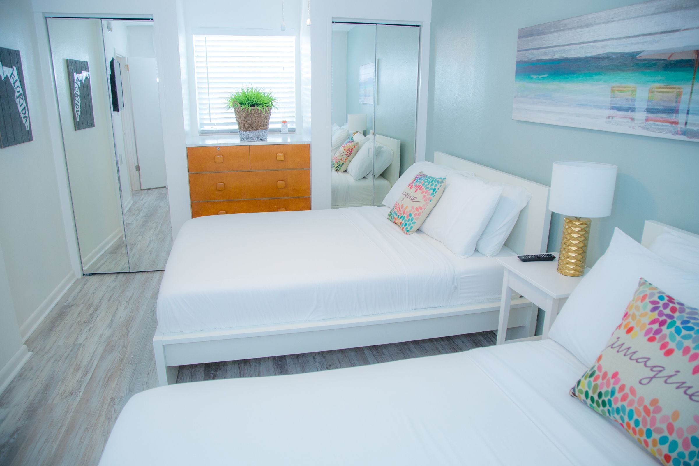 Un dormitorio con cama, cómoda, mesita de noche, lámpara y ventana con planta.