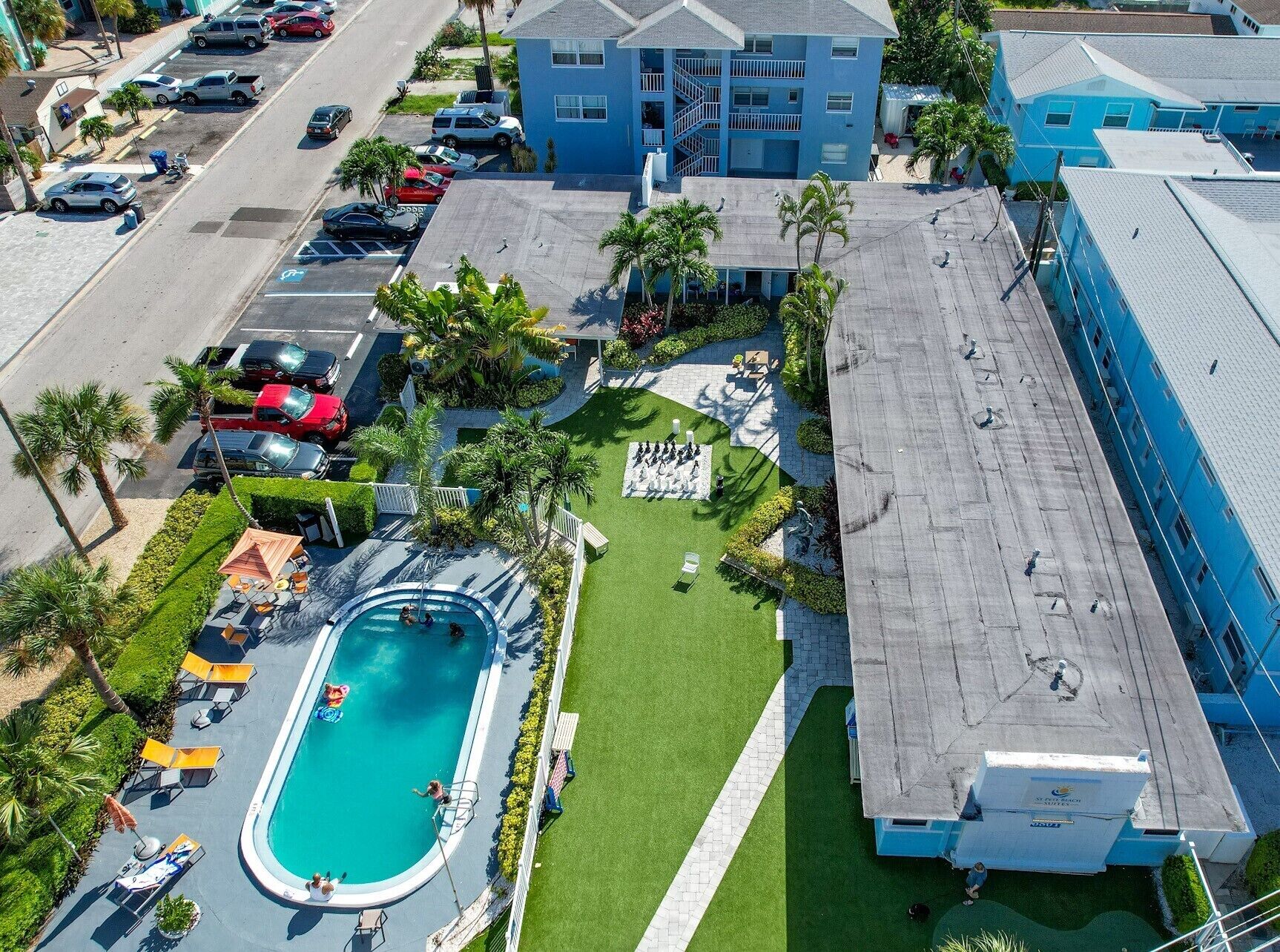 An aerial view of a hotel with a swimming pool, a parking lot, and a blue building with a staircase.